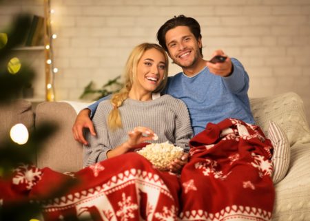 Young couple watching Christmas movie on couch under blanket