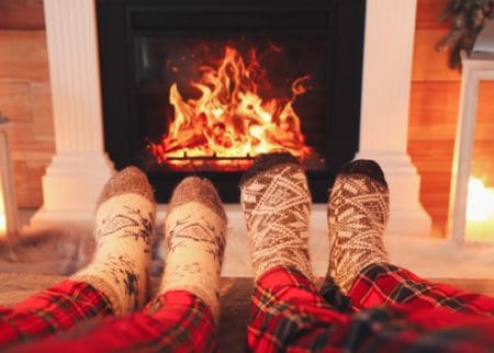 Couple in warm pjs and cozy socks sitting in front of fireplace watching fire
