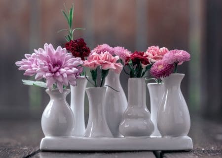 Different flowers in 6 small white vases grouped together on a table