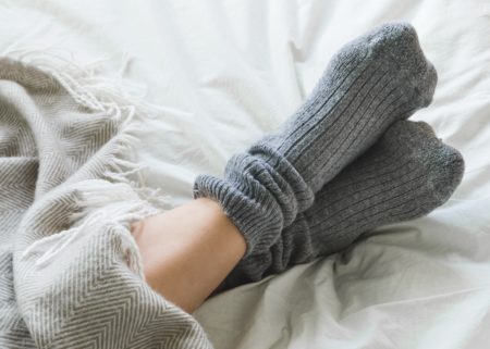 Feet Crossed With Gray socks On Bed Under Blanket