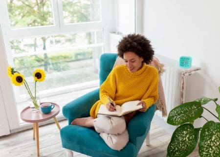 Portrait of a beautiful mixed race woman sitting in an armchair, next to a vase of sunflowers relaxing at home and writing a diary