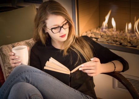 Young woman in glasses sitting on couch reading a book