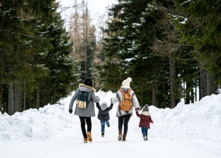 Family with 2 young children having festive walk in snowy woods