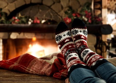 Women in cozy holiday sock and blanket sitting in front of fireplace